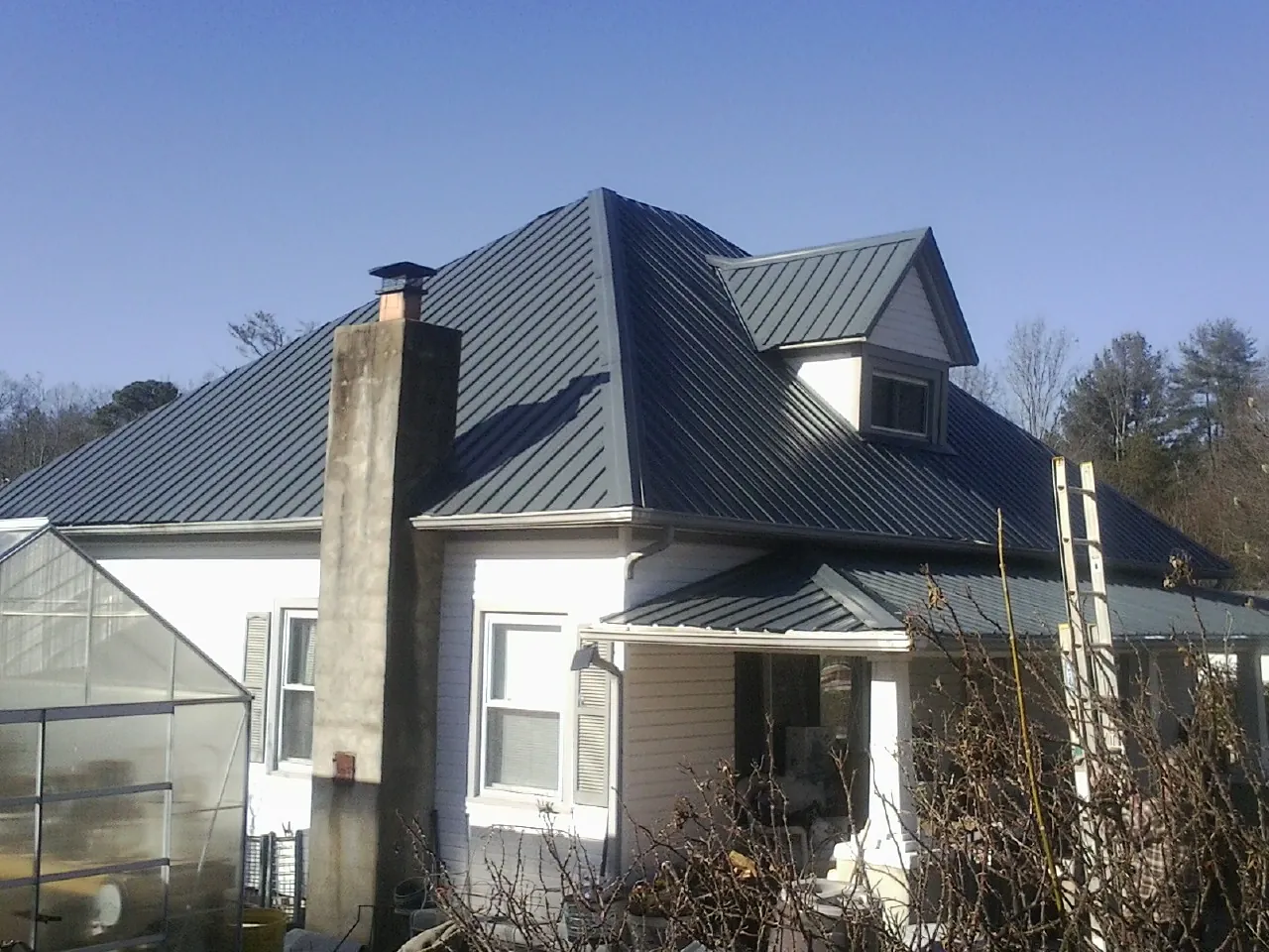 Dark blue standing seam metal roof on a white farmhouse with dormer — Slate & Tile Roof Repair by Roofing Brothers in Woodleaf
