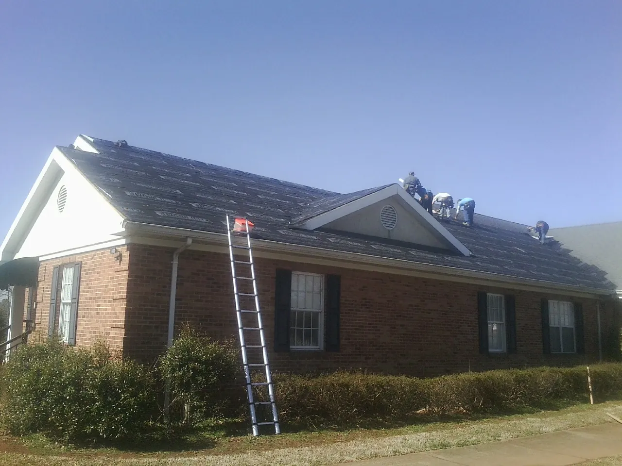 Crew tearing shingles off a brick ranch roof with a ladder set — Emergency Roof Repair work by our crew in Woodleaf