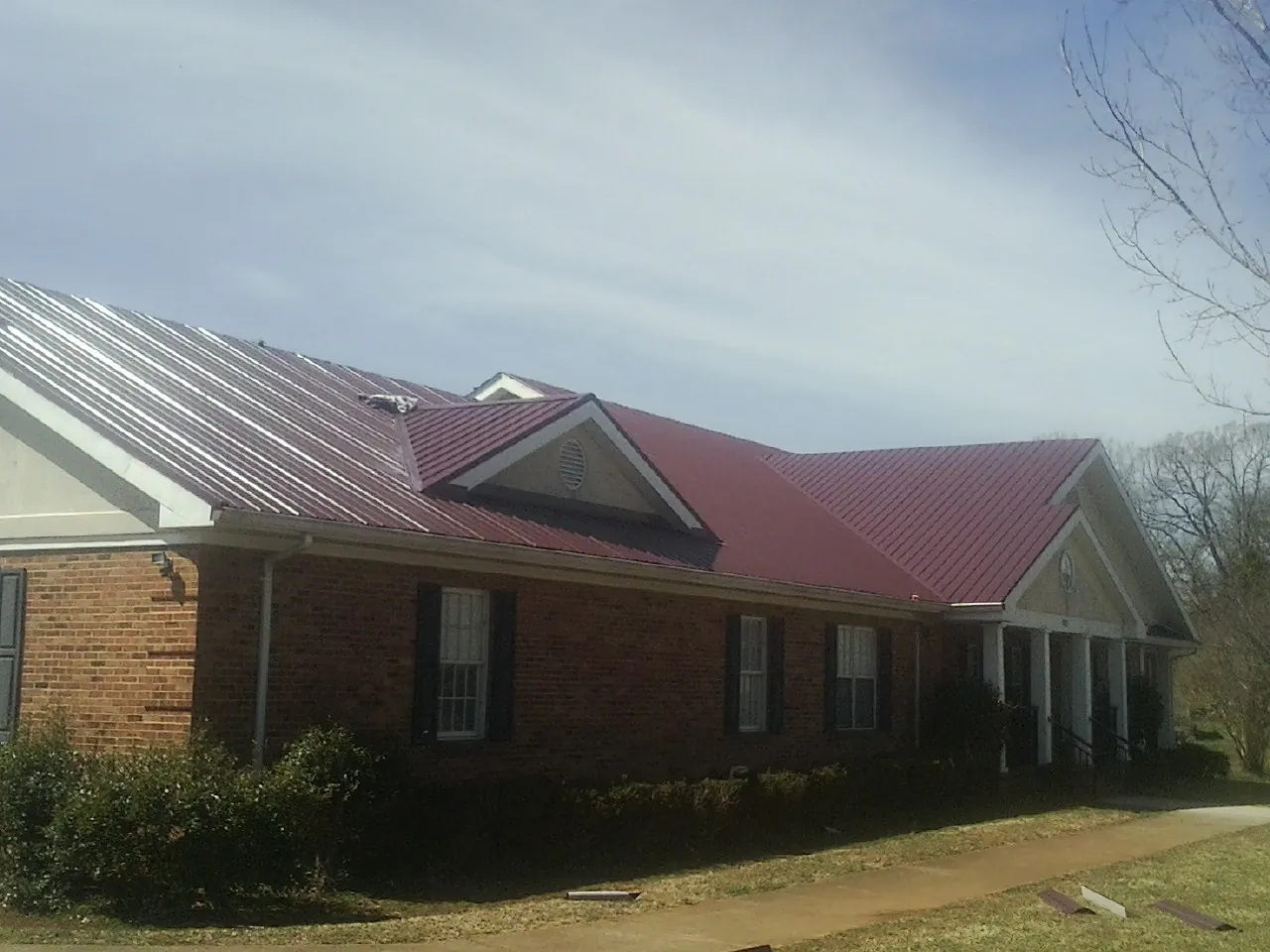 Red metal roof with gabled entries on a long brick building, from a Hail Damage Roof Repair job in Woodleaf