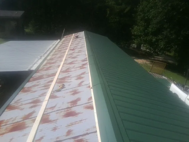 Old rusted panels beside newly installed green metal roofing — Wind Damage Roof Repair by Roofing Brothers in Woodleaf