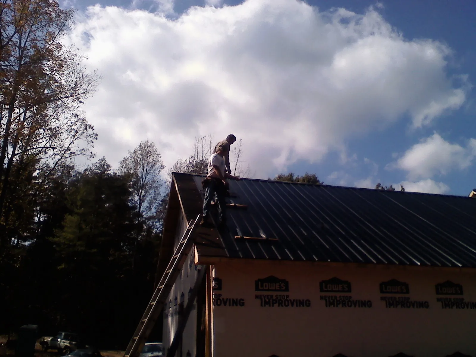 Roofer fastening dark metal panels high against a cloudy sky, from a Roof Inspection job in Woodleaf